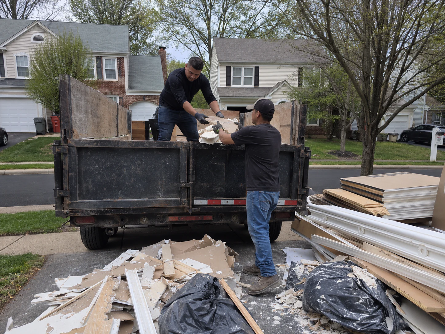Workers loading drywall, wood, and renovation debris into a hauling truck